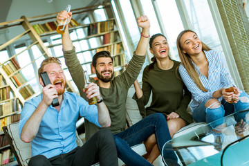 Group of young friends looking at the TV, drinking cider and having fun  in the room