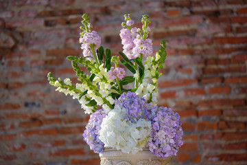 Minimalist white clay decorated flower pot with a spring bouquet featuring pastel hydrangeas, decorative element for a formal event or a wedding, with a terracotta color brick wall in the background