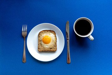 Breakfast concept. White plate with baked bread and egg and white coffee cup. Blue background.