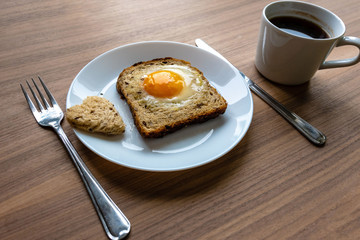 Breakfast concept. White plate with hearts of bread, baked bread and egg and white coffee cup. Wooden texture background.