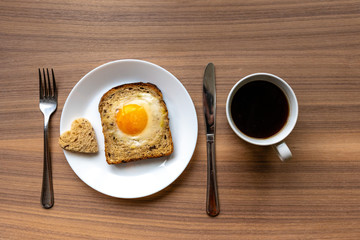 Breakfast concept. White plate with hearts of bread, baked bread and egg and white coffee cup. Wooden texture background.