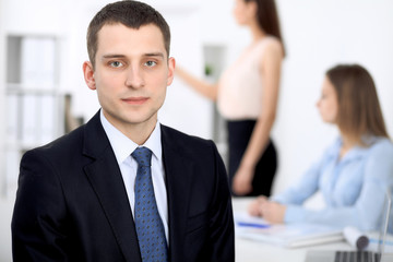 Portrait of a young business man  against a group of business people at a meeting