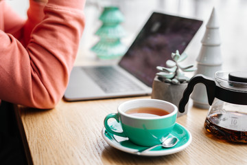 Red tea and man working at his laptop in cafe, green tea, plant, screen, hands.
