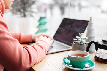Red tea and man working at his laptop in cafe, green tea, plant, screen, hands.