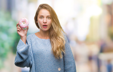 Young beautiful blonde woman eating sweet donut over isolated background scared in shock with a surprise face, afraid and excited with fear expression