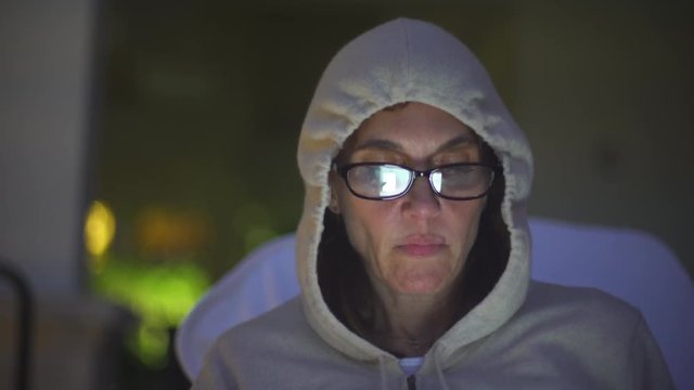 Woman at night in a hoodie and glasses bobbing her head to music.