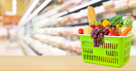 Shopping basket filled with fruits and vegetables on wood table with supermarket grocery store blurred defocused background with bokeh light