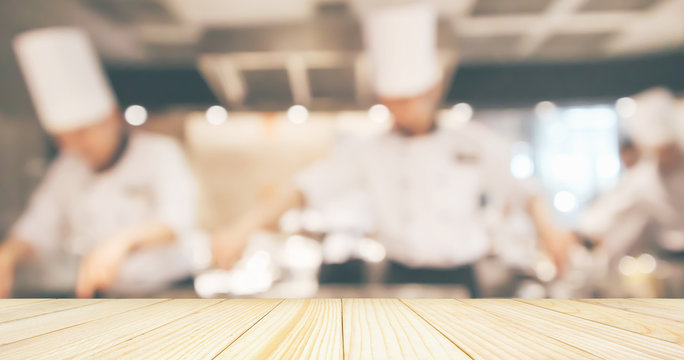 Empty Wood table top with Chef cooking in restaurant kitchen blurred defocused background