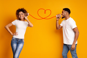 Young black couple with can phone on orange background