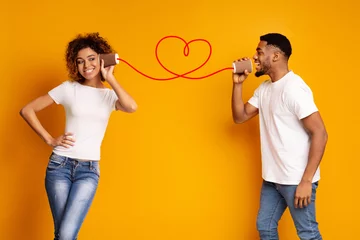 Fotobehang Young black couple with can phone on orange background © Prostock-studio