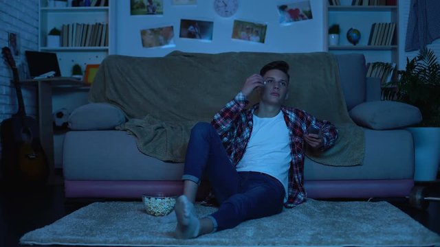 Bored teenager choosing tv channel eating popcorn and wasting time, couch potato