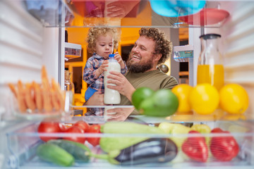 Father and son taking milk from fridge in late hours. Eating disorder concept.