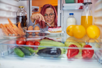 Woman standing in front of fridge an and eating cake cake. Picture taken from the inside of fridge. © chika_milan