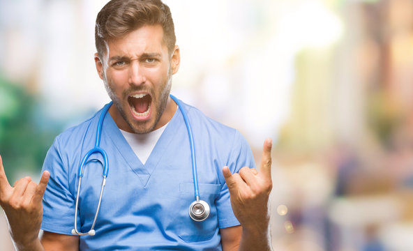 Young handsome doctor surgeon man over isolated background shouting with crazy expression doing rock symbol with hands up. Music star. Heavy concept.