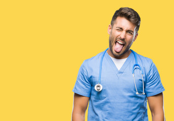 Young handsome doctor surgeon man over isolated background sticking tongue out happy with funny expression. Emotion concept.