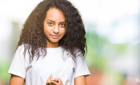 Young beautiful girl with curly hair wearing casual white t-shirt Hands together and fingers crossed smiling relaxed and cheerful. Success and optimistic