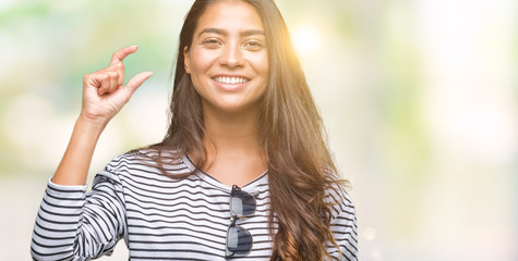 Young beautiful arab woman wearing sunglasses over isolated background smiling and confident gesturing with hand doing size sign with fingers while looking and the camera. Measure concept.