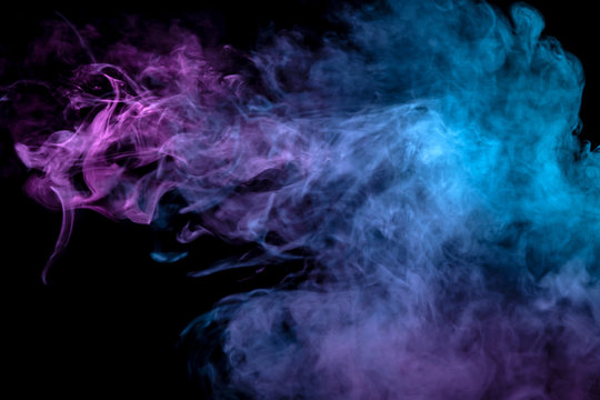 Multicolor, thick smoke, illuminated by colored in blue, purple and pink light against a dark black isolated background, welded with clubs and curls, rising from a steam of vape. Wind blow