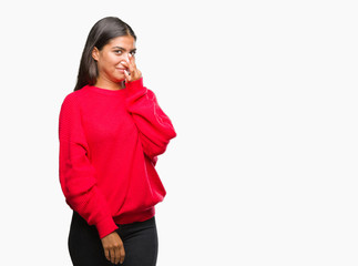 Young beautiful arab woman wearing winter sweater over isolated background smelling something...