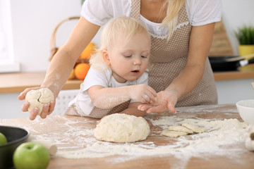 Little girl and her blonde mom in beige aprons  playing and laughing while kneading the dough in kitchen. Homemade pastry for bread, pizza or bake cookies. Family fun and cooking concept