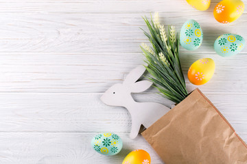 Easter composition with craft paper package, colorful easter eggs, decorative wooden bunny and flowers. Flat lay, top view, copy space