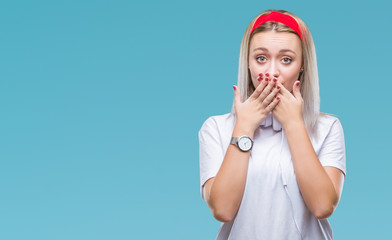 Young blonde woman wearing headphones listening to music over isolated background shocked covering mouth with hands for mistake. Secret concept.