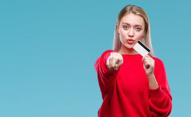 Fototapeta na wymiar Young blonde woman holding credit card over isolated background pointing with finger to the camera and to you, hand sign, positive and confident gesture from the front