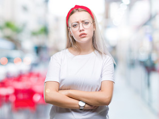 Young blonde woman wearing glasses over isolated background skeptic and nervous, disapproving expression on face with crossed arms. Negative person.