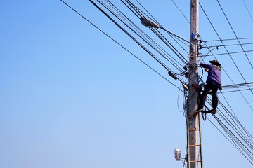 Low angle view of electrician on wooden staircase are working to repair electrical system on electric pole against blue sky background