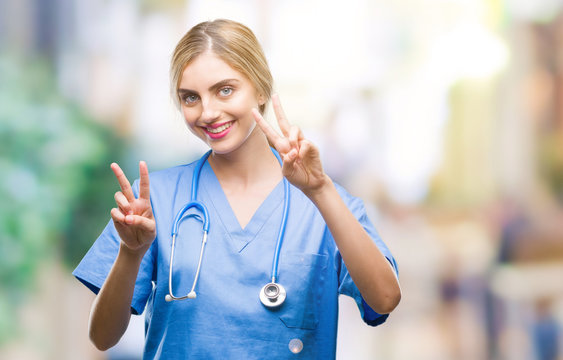 Young beautiful blonde doctor surgeon nurse woman over isolated background smiling looking to the camera showing fingers doing victory sign. Number two.