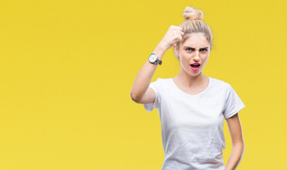 Young beautiful blonde woman wearing white t-shirt over isolated background angry and mad raising fist frustrated and furious while shouting with anger. Rage and aggressive concept.