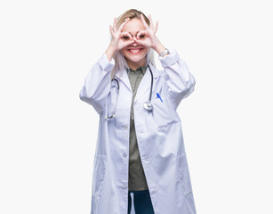 Young blonde doctor woman over isolated background doing ok gesture like binoculars sticking tongue out, eyes looking through fingers. Crazy expression.