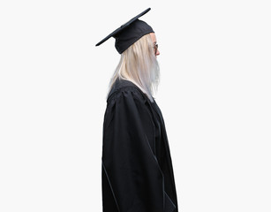 Young blonde woman wearing graduate uniform over isolated background looking to side, relax profile...