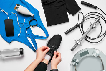 Young woman in sporting leggings laces sneakers, preparing for training. Accessories for sports on white background flat lay top view.