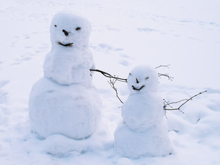 Two funny snowmen, big and small. Parent and child. Both smiling. The parent only has one arm, possibly disabled. White background.
