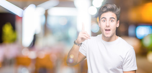 Young handsome man wearing white t-shirt over isolated background pointing finger up with successful idea. Exited and happy. Number one.