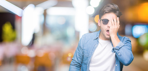 Young handsome man wearing sunglasses over isolated background Yawning tired covering half face, eye and mouth with hand. Face hurts in pain.