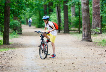 Child teenager on  bicycle ride in  forest at spring or summer. Happy smiling Boy cycling outdoors in blue helmet. Active lifestyle, hobby