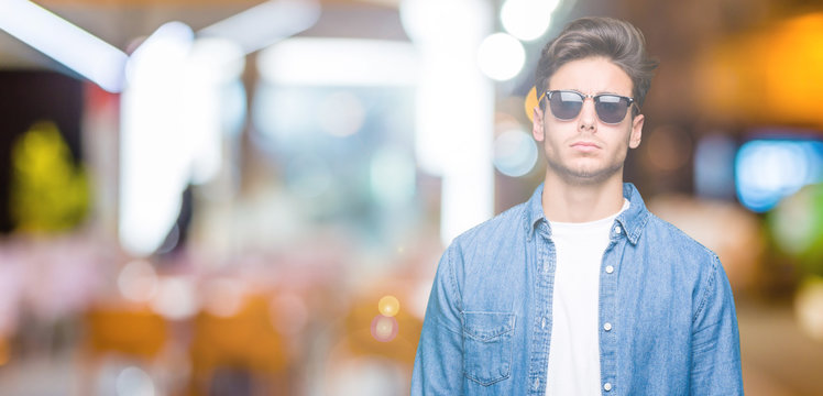 Young handsome man wearing sunglasses over isolated background skeptic and nervous, frowning upset because of problem. Negative person.