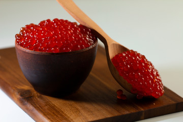 red caviar in a ceramic dish on a wooden platform on a white background