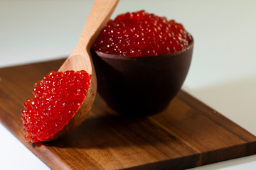 red caviar in a ceramic dish on a wooden platform on a white background