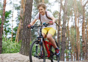 Obraz premium Child teenager in white t shirt and yellow shorts on bicycle ride in forest at spring or summer. Happy smiling Boy cycling outdoors Active lifestyle, hobby