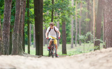 Child teenager in white t shirt and yellow shorts on bicycle ride in forest at spring or summer. Happy smiling Boy cycling outdoors Active lifestyle, hobby