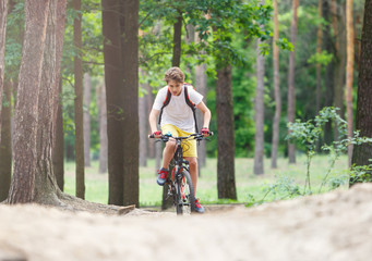Obraz premium Child teenager in white t shirt and yellow shorts on bicycle ride in forest at spring or summer. Happy smiling Boy cycling outdoors Active lifestyle, hobby