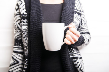 Female hand holding white cup in black patterned sweater background. Copy space