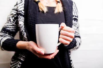 Female hand holding white cup in black patterned sweater background. Copy space