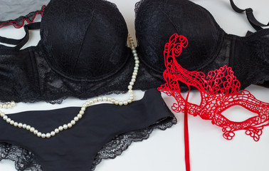Sexy female black lace underwear. Bra, panties, lace red mask and pearls on a white background.