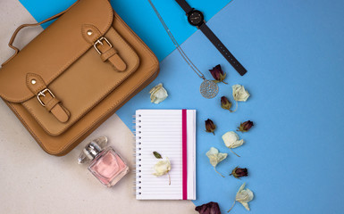 Women's accessories. Notepad, women's cutie, wrist watches, perfume, necklace and flowers on a blue and gray background