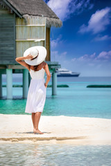 Fototapeta na wymiar Frau in weißem Sommerkleid steht am Strand der Malediven und genießt den Ausblick auf den türkisen Ozean