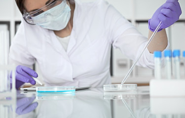 Close-up of professional female scientist in protective eyeglasses making experiment with reagents in laboratory. Medicine and research concept